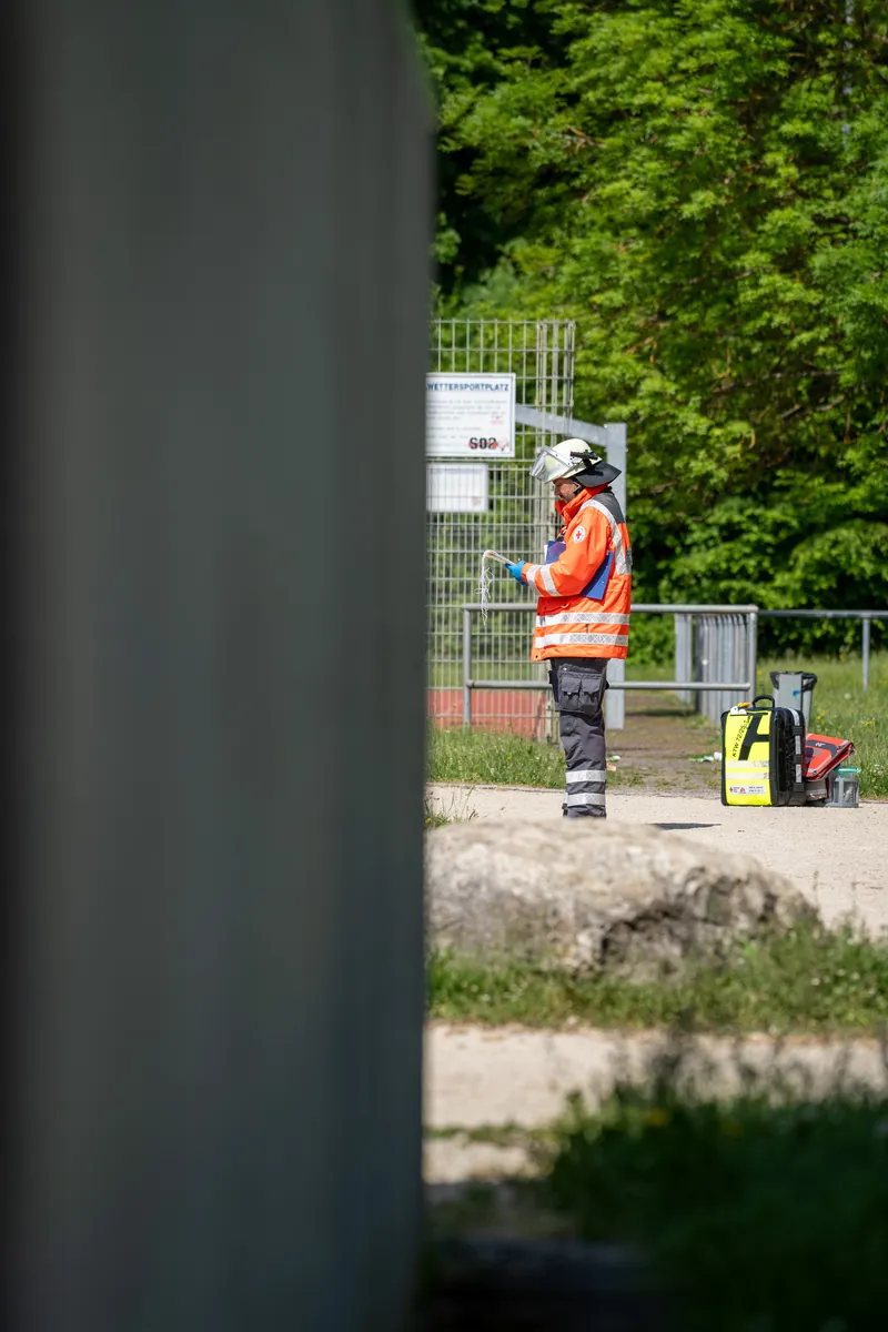 Durch einen Spalt beobachtet: Einsatzkraft mit Notfallrucksack am Sportplatz