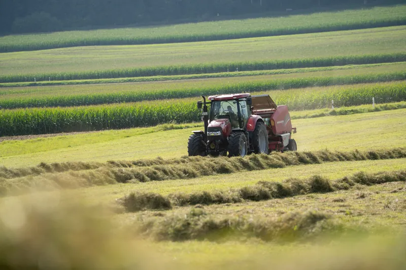 Roter Traktor mit Rundballenpresse auf dem Feld