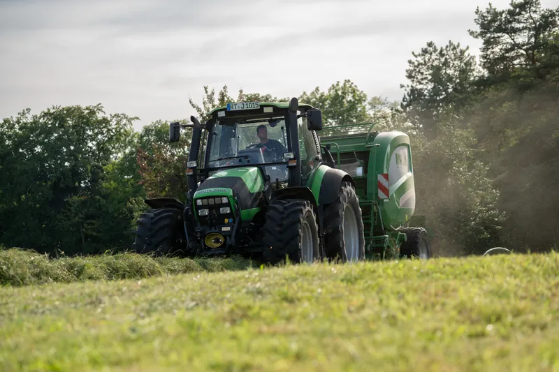 Grüner Traktor mit Rundballenpresse im Staub