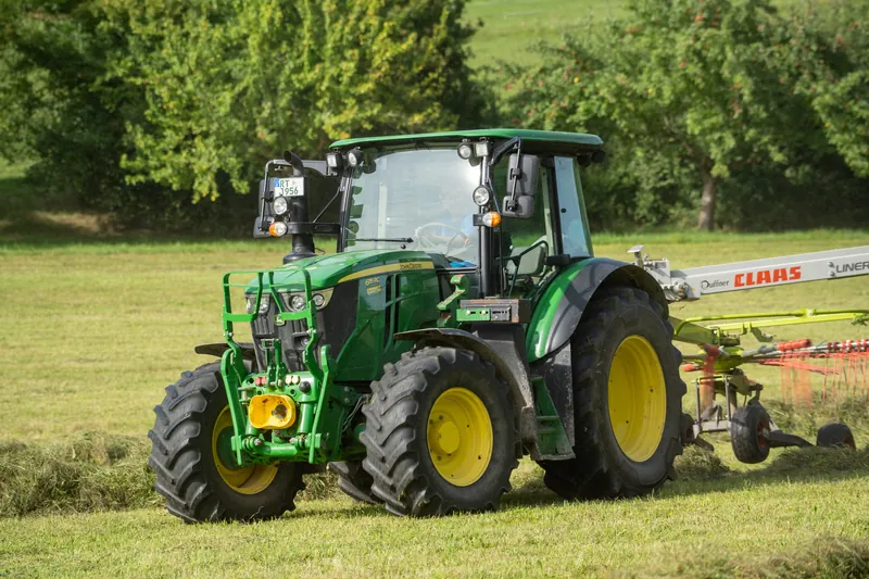 Grüner Traktor mit Schwader auf der Wiese